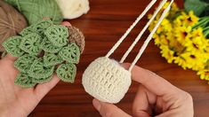 two hands holding small crocheted balls of yarn next to yellow and green flowers