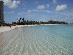 people are swimming in the clear blue water at an empty beach on a sunny day