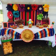 a table topped with lots of food under a colorful tent covered in flowers and ribbons