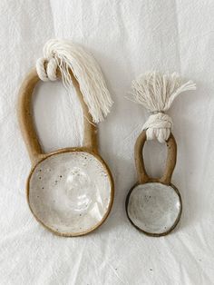 two ceramic bowls with tassels on them sitting on a white cloth covered surface