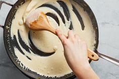 a person stirring something in a skillet with a wooden spoon