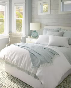 a bed with white linens and pillows in a bedroom next to two large windows