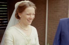 a woman in a wedding dress smiles as she stands next to a man wearing a suit and tie