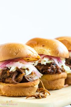 three pulled pork sandwiches on a cutting board