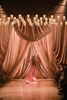 a fashion show with people sitting on the floor and one person standing in front of an open curtain