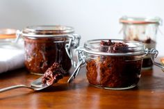 three jars filled with food sitting on top of a wooden table next to a spoon