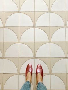 a person wearing red shoes standing in front of a white tile wall with circles on it