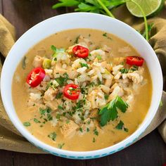 a white bowl filled with chicken and rice soup on top of a wooden table next to a green napkin