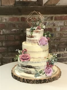 a three tiered cake with flowers and leaves on a wooden stand in front of a brick wall