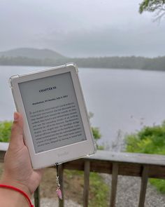 a person holding up an electronic device in front of a body of water on a cloudy day