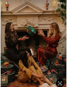 three women sitting on the floor in front of a fire place and one is holding a green present