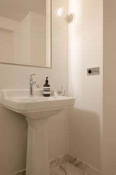 a white bathroom sink sitting under a mirror next to a wall mounted faucet