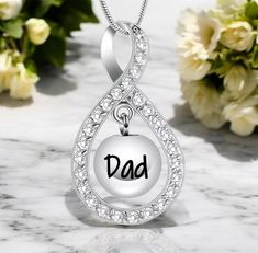 a necklace with the word dad written on it and flowers in the back ground behind it