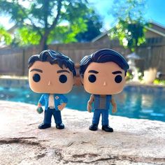 two figurines are standing next to each other near a pool with trees in the background