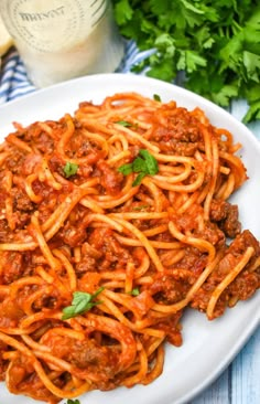 spaghetti with meat sauce and parsley on a white plate next to some parsley