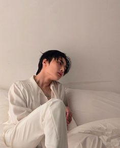 a man sitting on top of a white bed covered in sheets and pillows with his head resting on the pillow