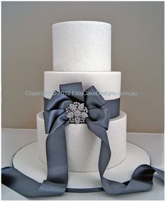 a three tiered white cake with grey ribbons