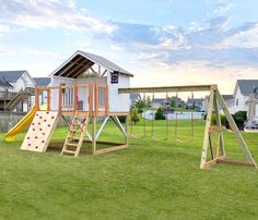 a wooden play set with swings and slides in the grass next to some houses