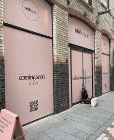 a person sitting on the sidewalk in front of some pink storefronts and signs