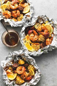 grilled shrimp and corn on the cob in tin foil next to a bowl of dipping sauce