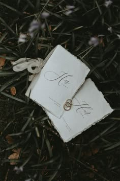 two wedding rings laying on top of an envelope in the grass with flowers around them