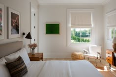 a bedroom with white bedding and pictures hanging on the wall next to it's windows