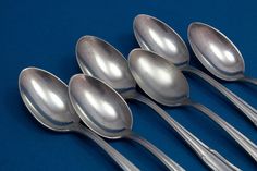 five silver spoons are lined up on a blue surface