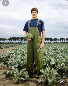 a young man standing in a field holding vegetables