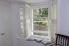 an open window with white shutters and pillows