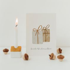 a white candle and some nuts next to a card with a gift box on it