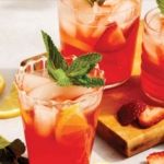 two glasses filled with lemonade and strawberries on top of a cutting board next to sliced lemons