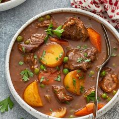 two bowls of beef stew with carrots, potatoes and parsley on the side