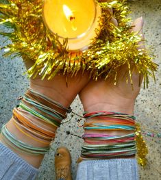 two hands holding a lit candle surrounded by bracelets