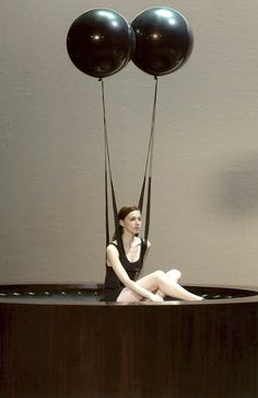 a woman sitting on top of a piano with two black balloons attached to her legs