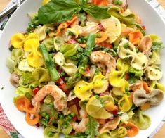 a white bowl filled with pasta and vegetables on top of a wooden table next to silverware