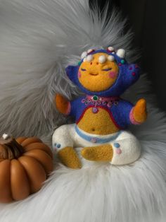 a stuffed animal sitting next to a small pumpkin on a white fur covered surface,