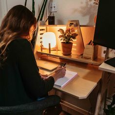 a woman sitting at a desk writing on a notepad in front of a computer monitor