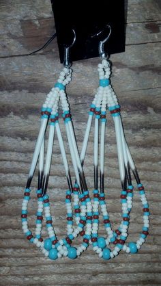 two pairs of white and blue beaded earrings on a wooden table next to a cell phone