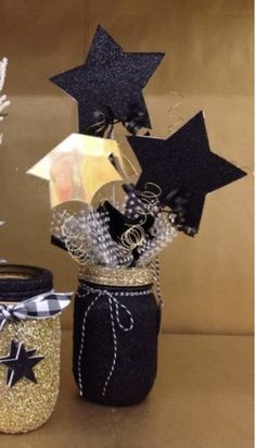 three mason jars decorated with stars and ribbons, one is black and the other is gold