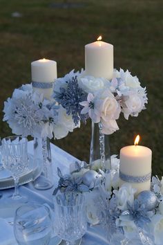 a table topped with white flowers and candles next to plates filled with silverware on top of a grass covered field