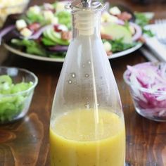 a glass bottle filled with liquid sitting on top of a wooden table next to plates of salad