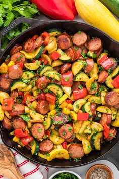 a skillet filled with sausages, peppers and zucchini next to other ingredients