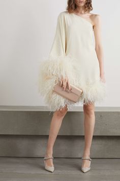 a woman in a white dress with feathers on the skirt and one hand holding a pink purse