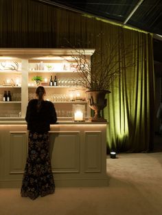 a woman standing in front of a bar with bottles on the shelves and candles behind her