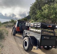 two jeeps parked on the side of a dirt road next to trees and water