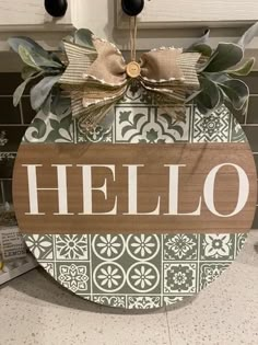 a sign that says hello hanging on the front of a kitchen counter with tile behind it