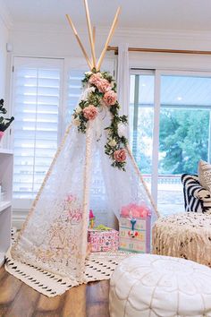 a teepee is decorated with pink flowers and greenery in front of a window