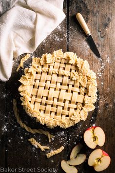 an apple pie on a wooden table with some sliced apples and a knife next to it