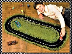 a young boy laying on the floor next to a green rug with cars and trucks