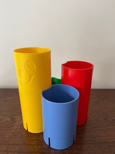 three different colored plastic cups sitting on top of a wooden table next to each other